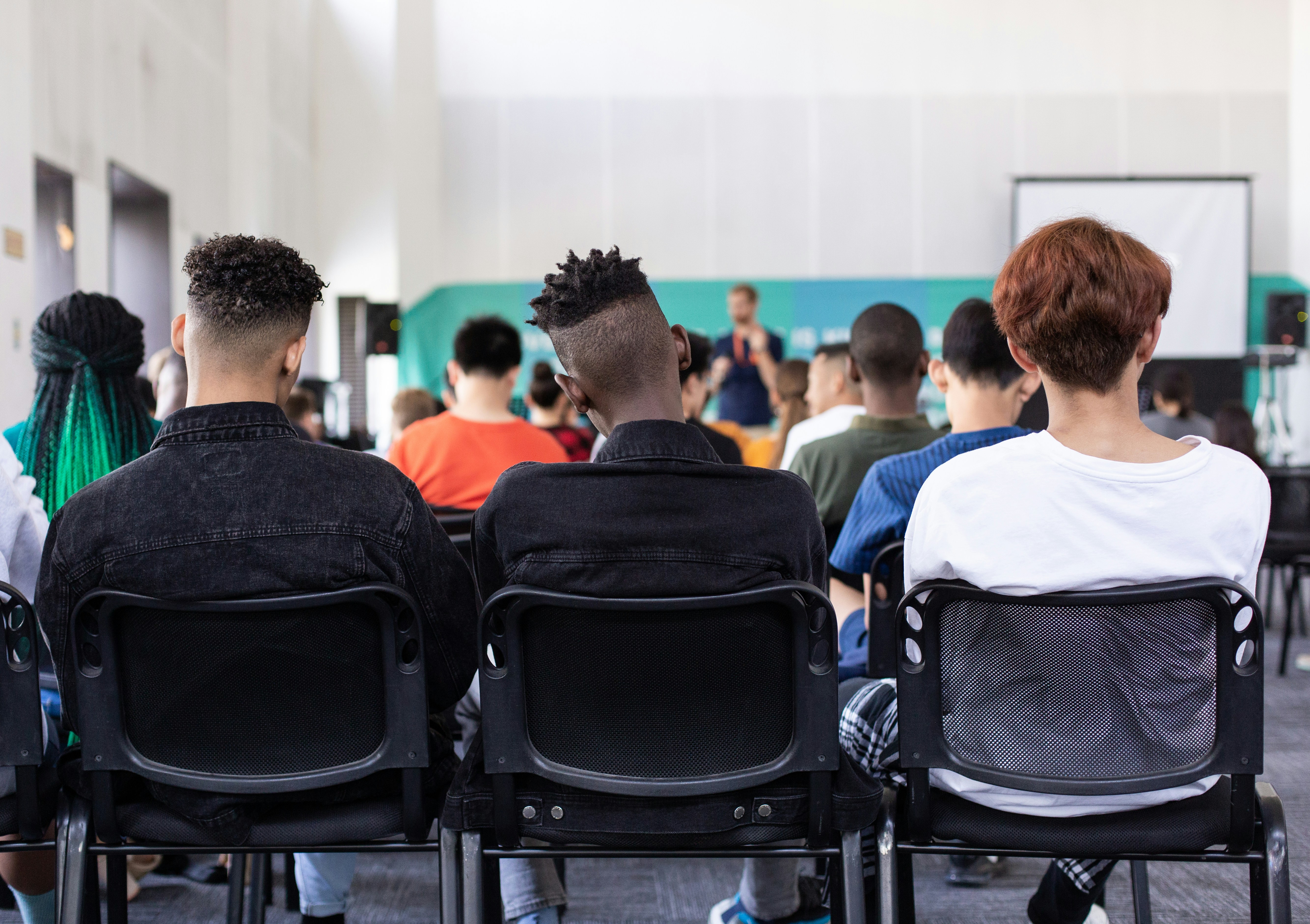 The backs of three teenage boys' heads as they listen to a talk in a large classroom