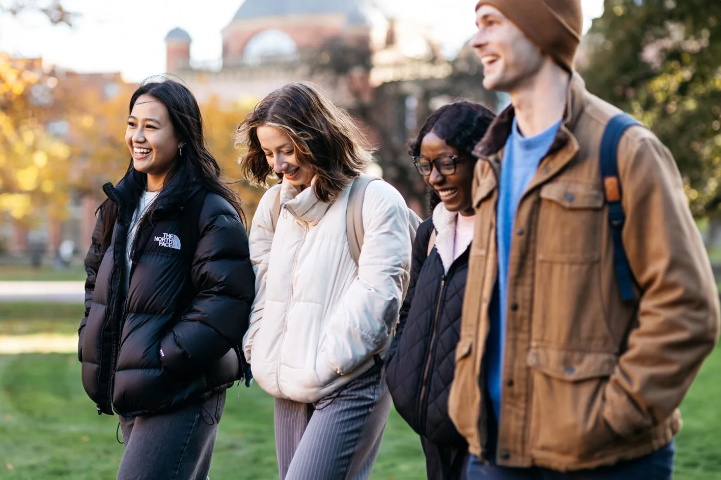 Four students walking together smiling with an autumnal-looking Chancellor's Court in the background