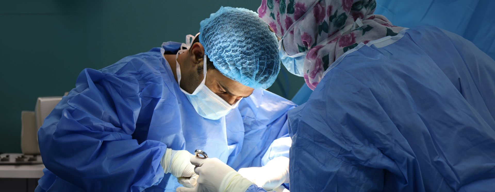 Surgeons wearing blue theatre gowns, gloves and skull caps performing an operation