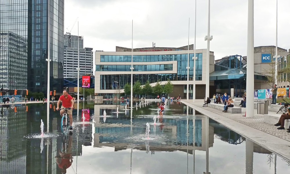A man rides a bicycle through a shallow pool in front of Symphony Hall, Birmingham