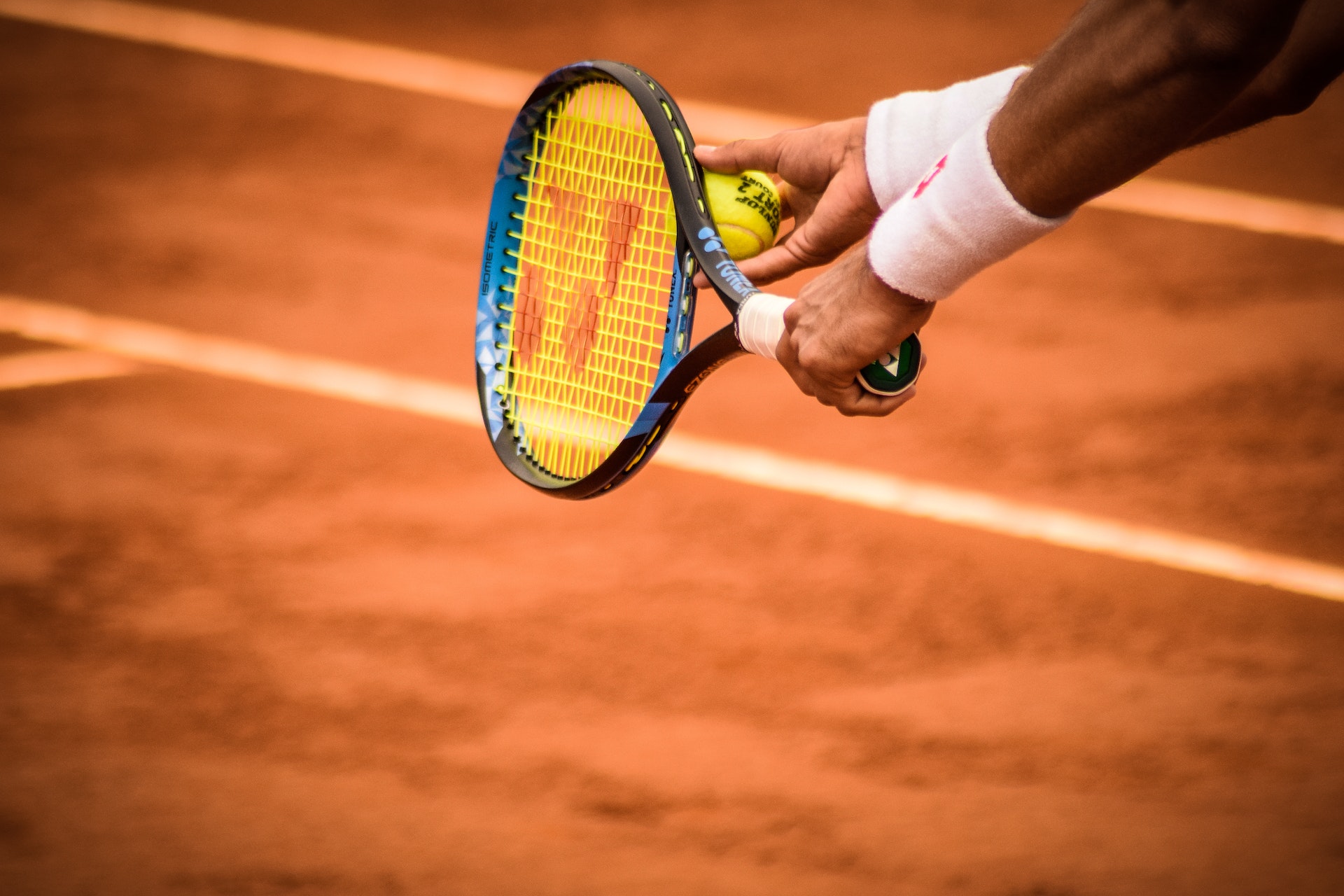 Tennis player preparing to serve, holding racquet and ball, against a clay court background