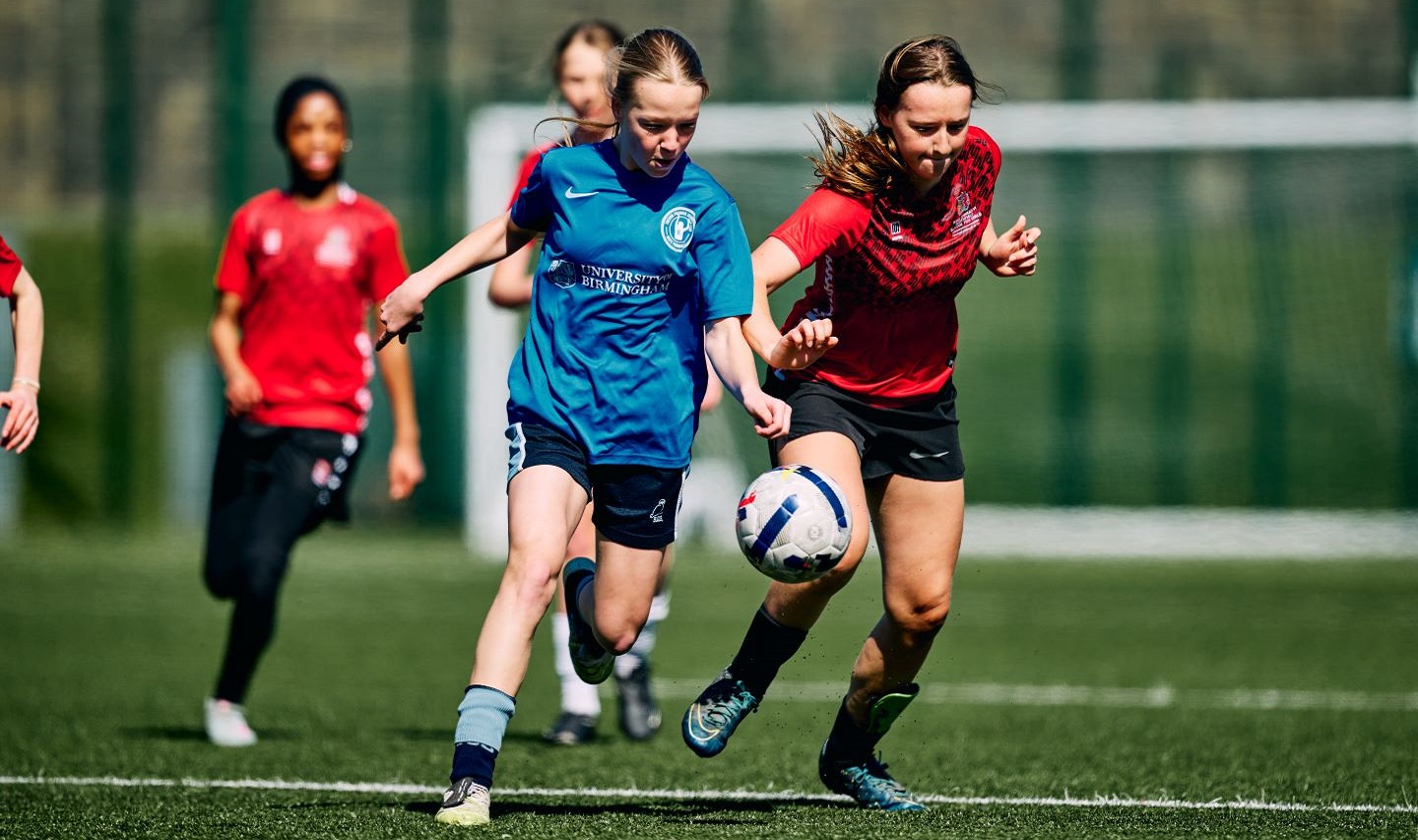 Two girls challenge for the ball in a football match