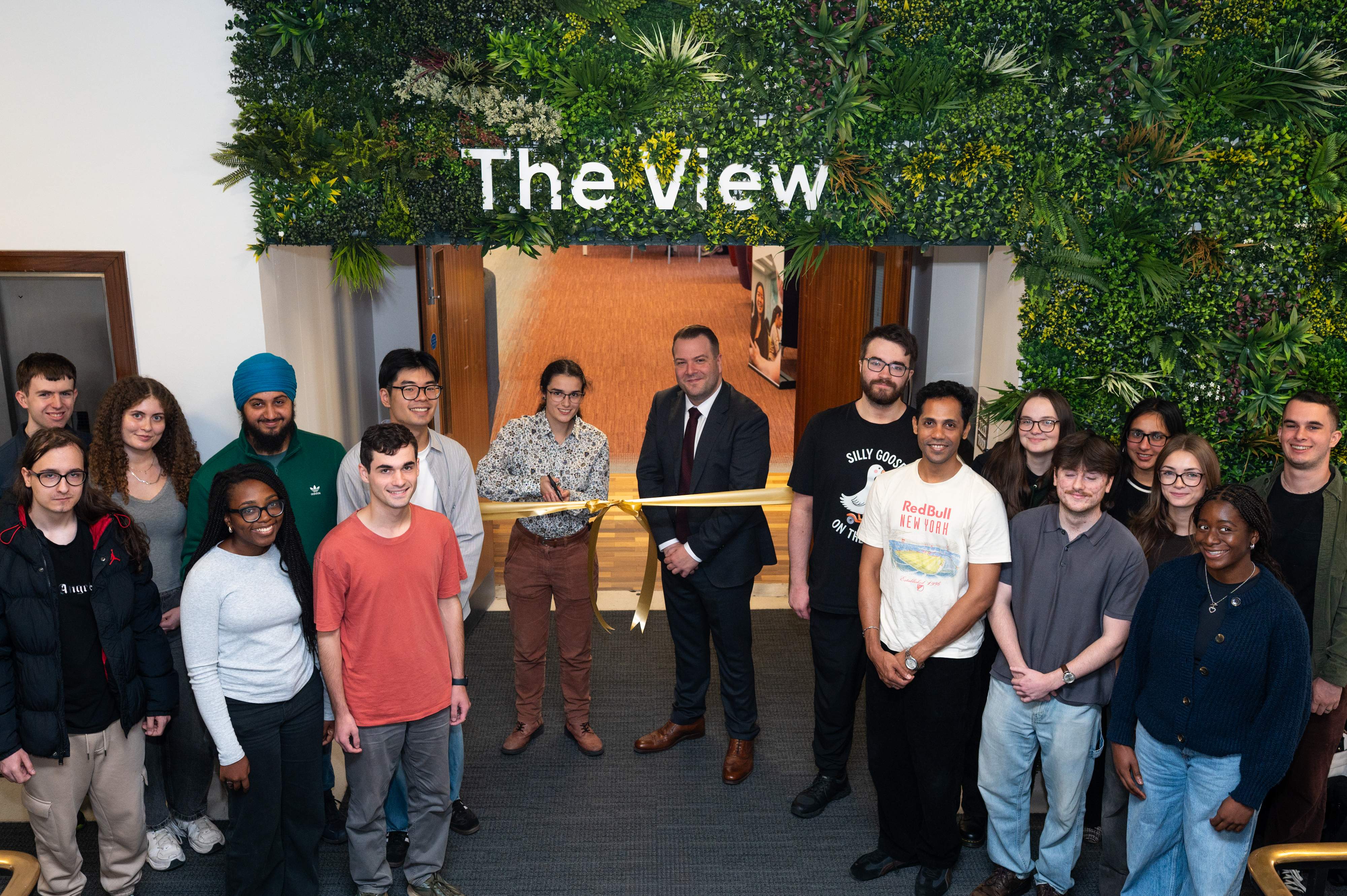 A group of students and a professor stand below a sign that says The View with a gold ribbon.