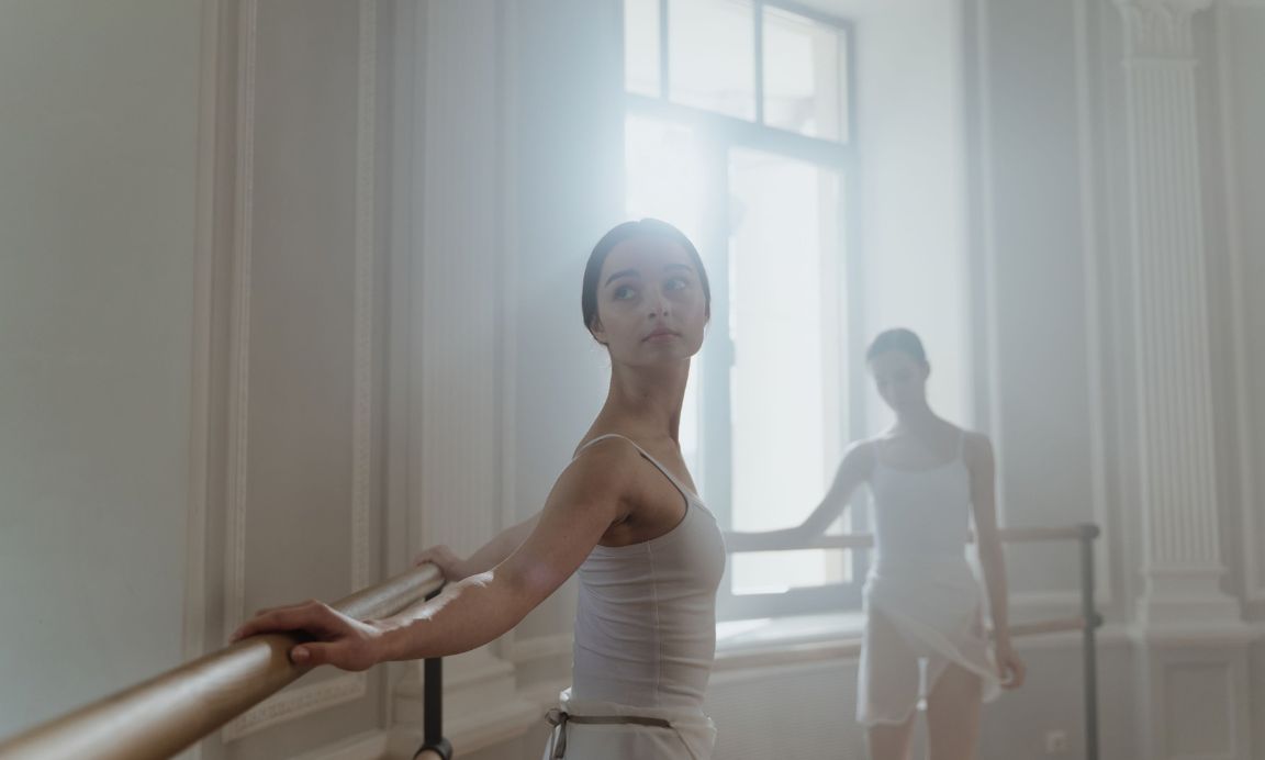 Two female ballet dancers gracefully practicing in a sunlit ballet studio. 