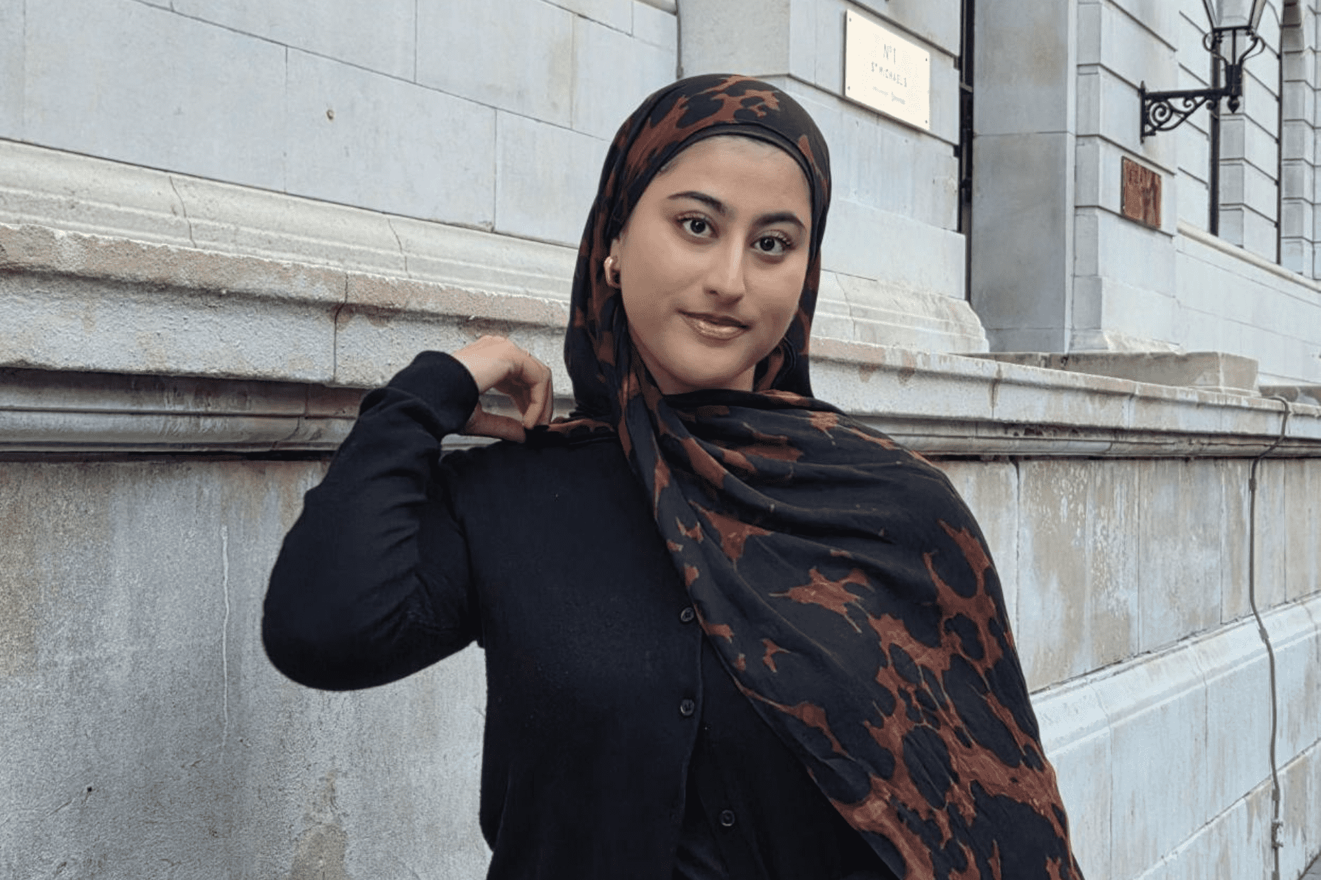 Student Maimoona smiles in front of a white brick building