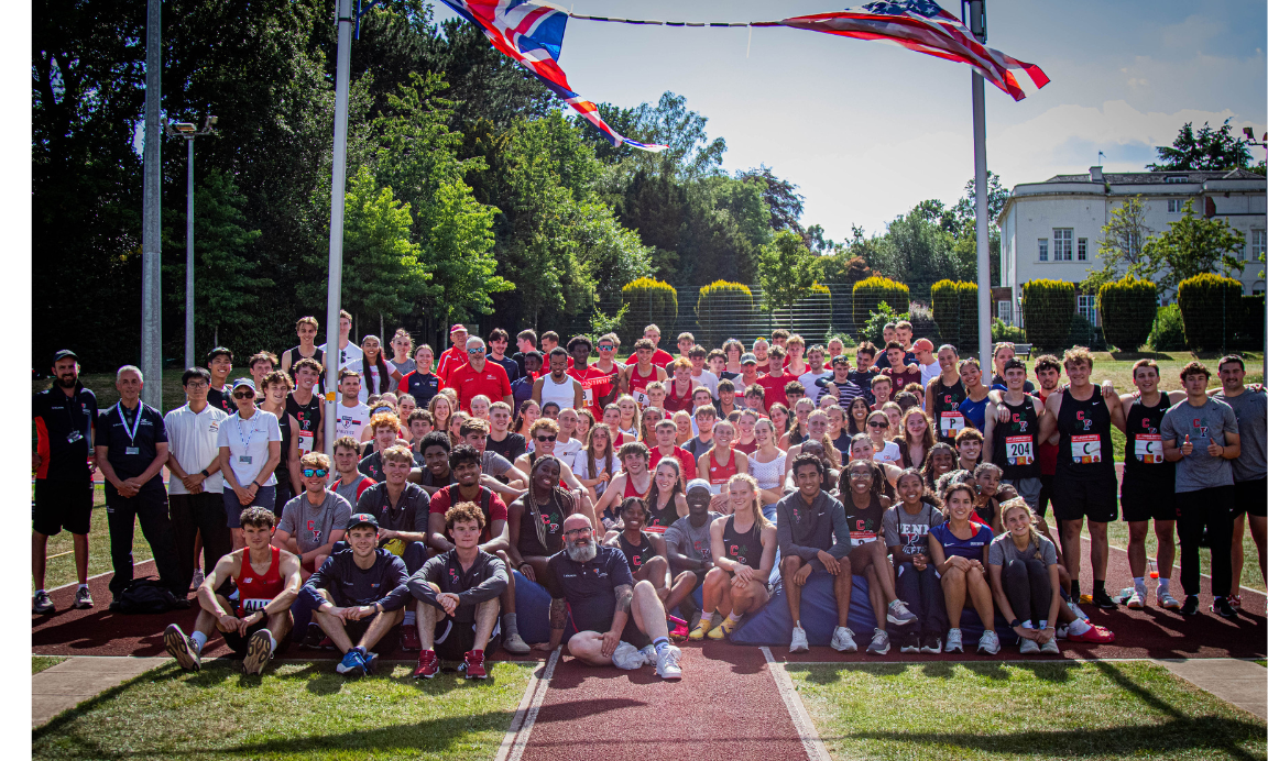 A group of students and staff wearing athletic gear are sat together under the UK and USA flags