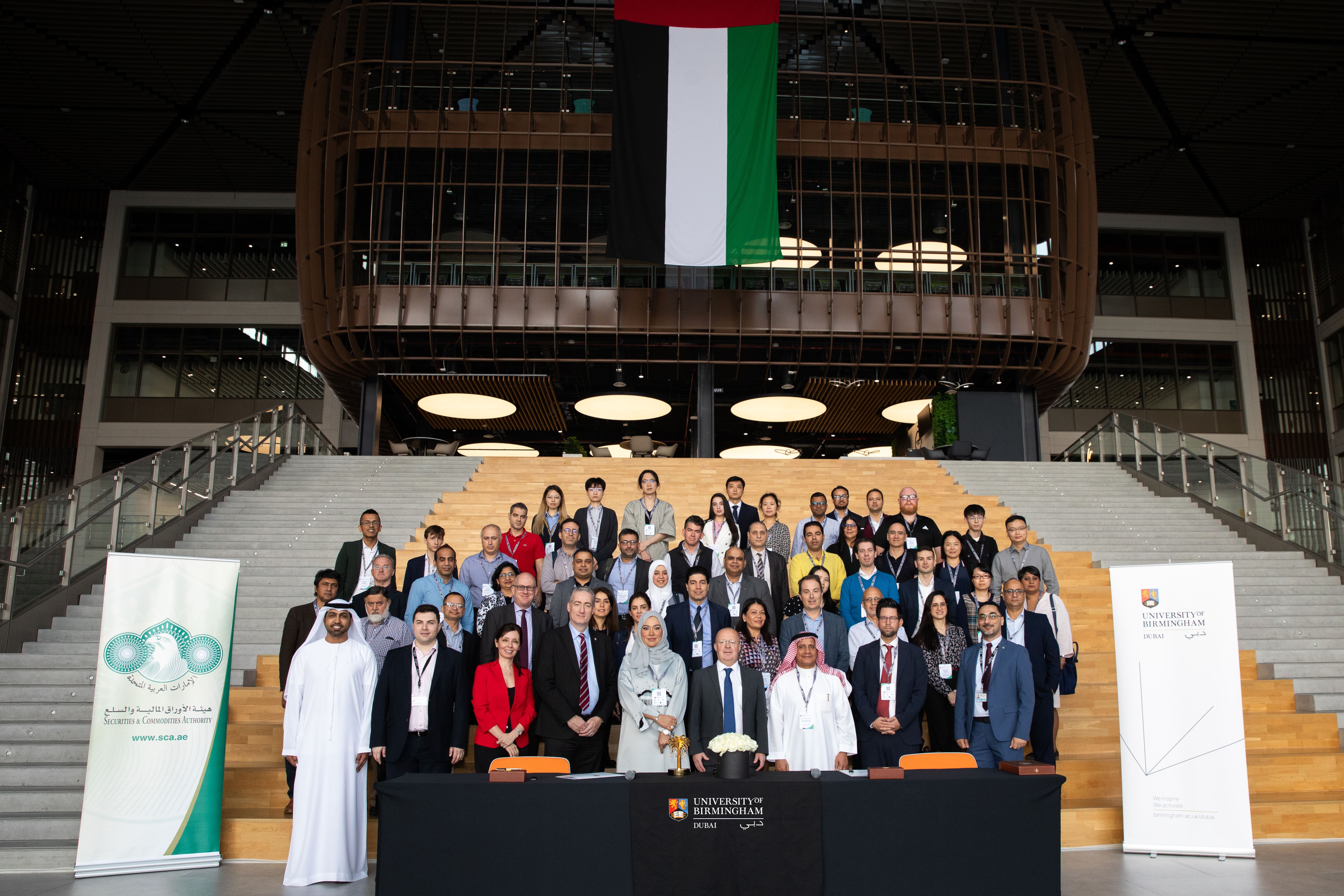 Large group of people standing on steps beneath a UAE flag