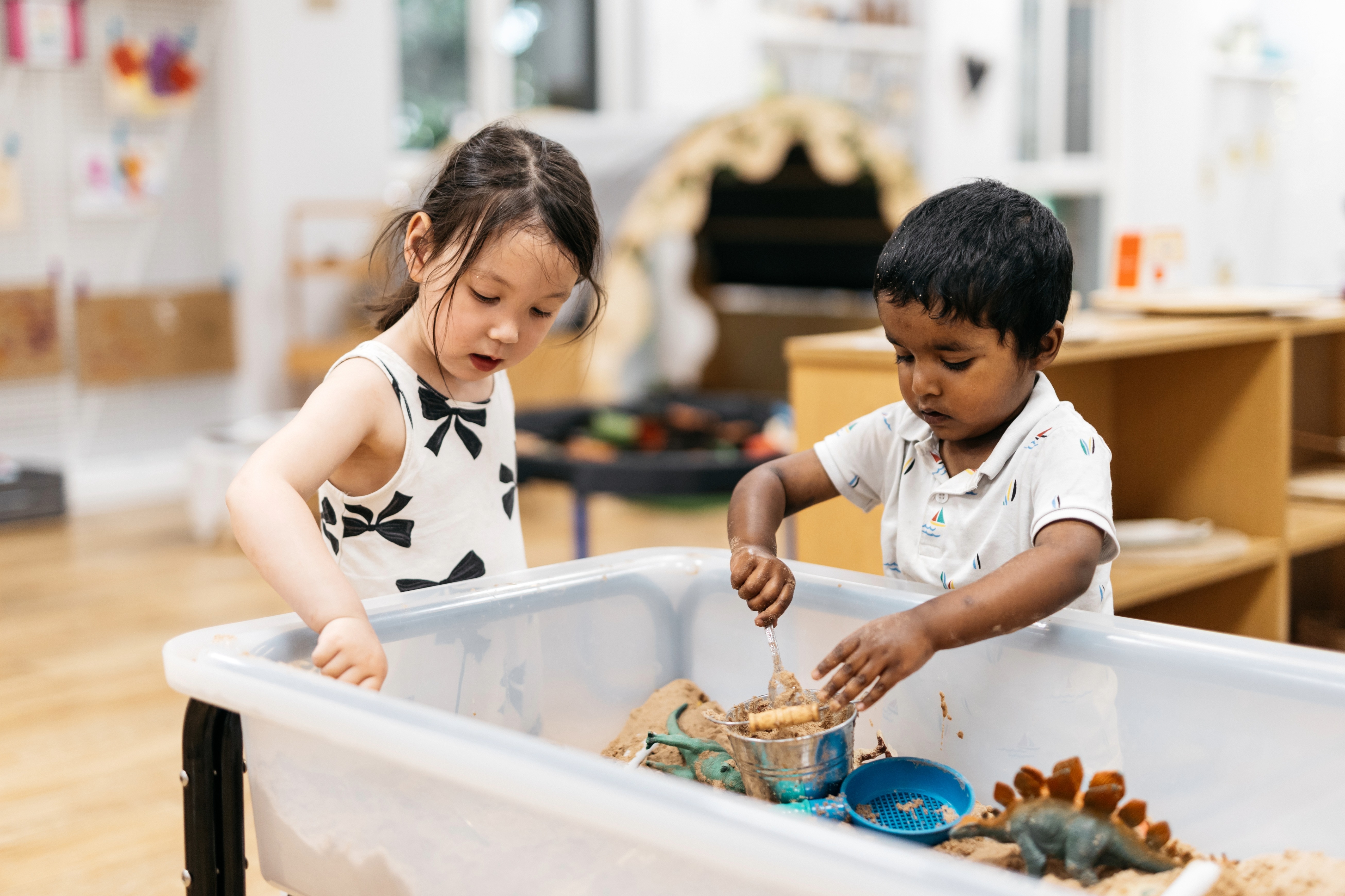 Two young children playing with sand indoors.