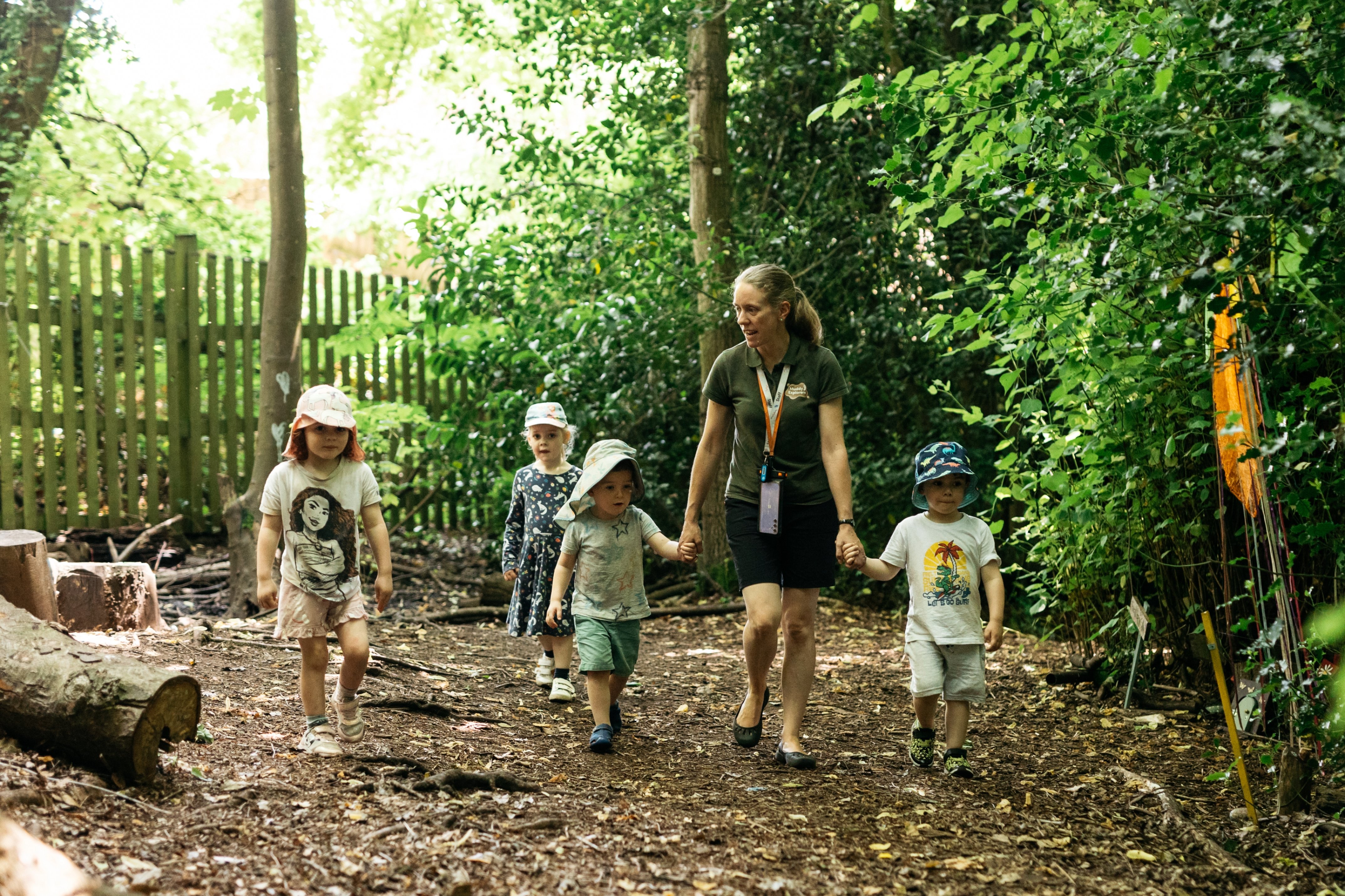 A member of staff hand-in-hand with children exploring the forest
