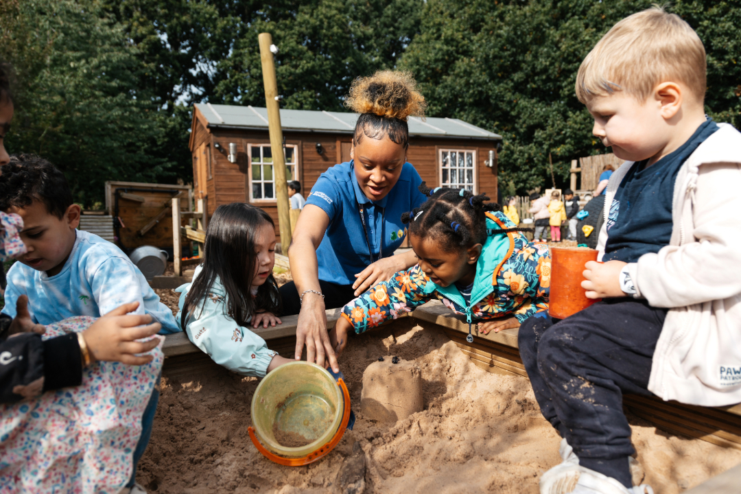A member of staff playing with children in the sandpit outside