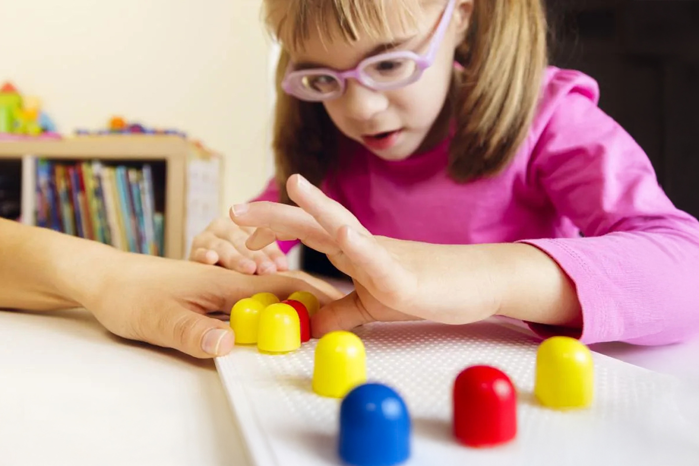 A visually impaired little girl wearing glasses doing a classroom exercise with coloured shapes