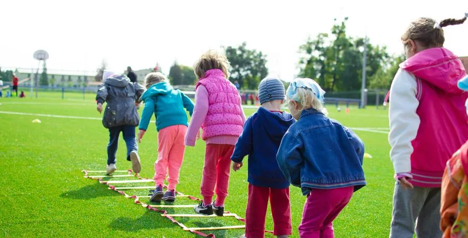 Six children playing hopscotch on a playground field.