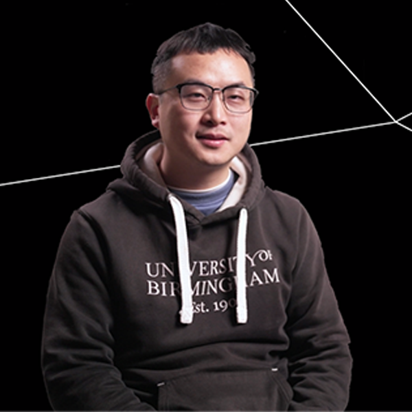 Wei Wu sitting down in front of a black background smiling wearing a UOB hoodie.
