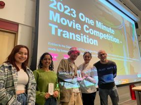 Winners of the One Minute Movie competition with their awards standing in front of a projection screen