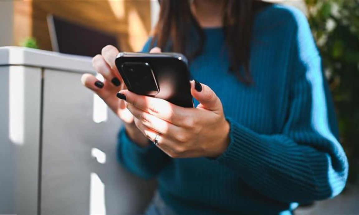 A woman in a blue jumper and painted nails using a smartphone.