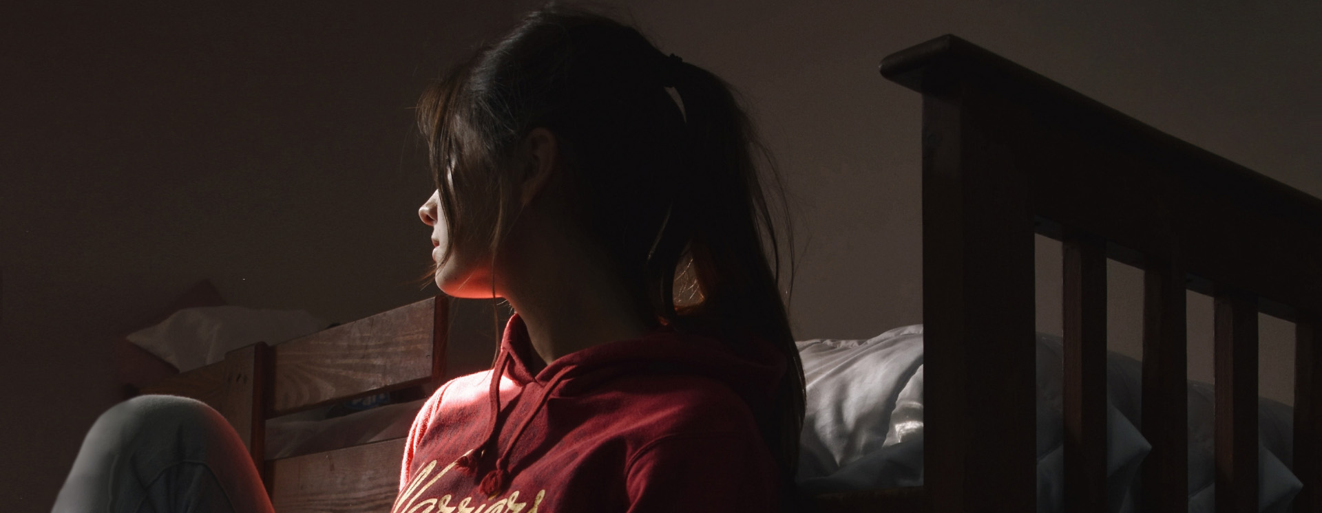 Woman sitting on the floor, against her bed in the dark.