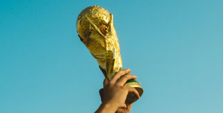 A pair of hands holding up the World Cup trophy against a bright blue sky.