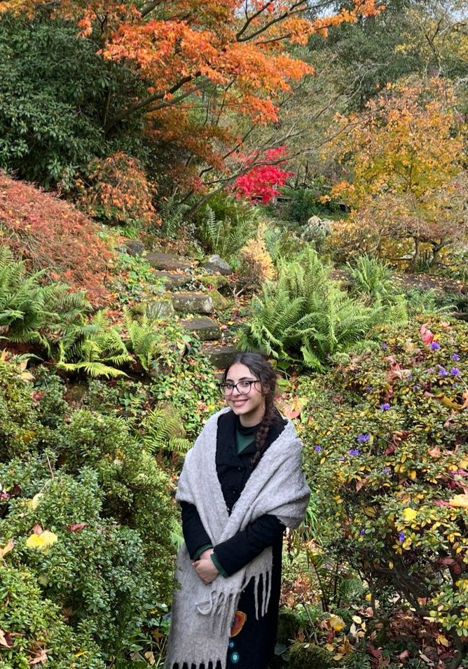 Woman stood smiling amidst colourful garden plants and shrubs.