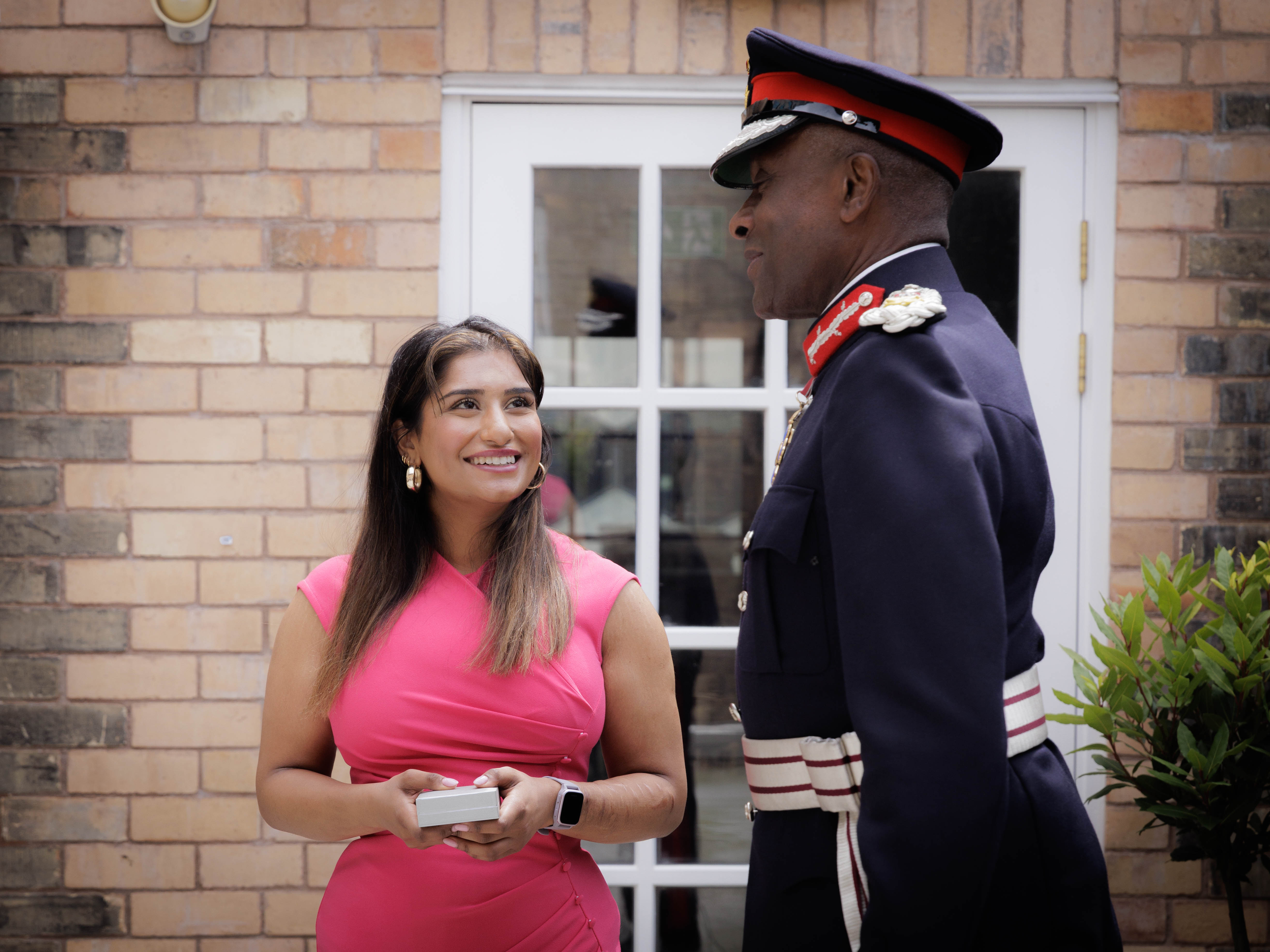 Zaynab holds a small box while smiling and talking to the uniformed Lord-Lieutenant of the West Midlands