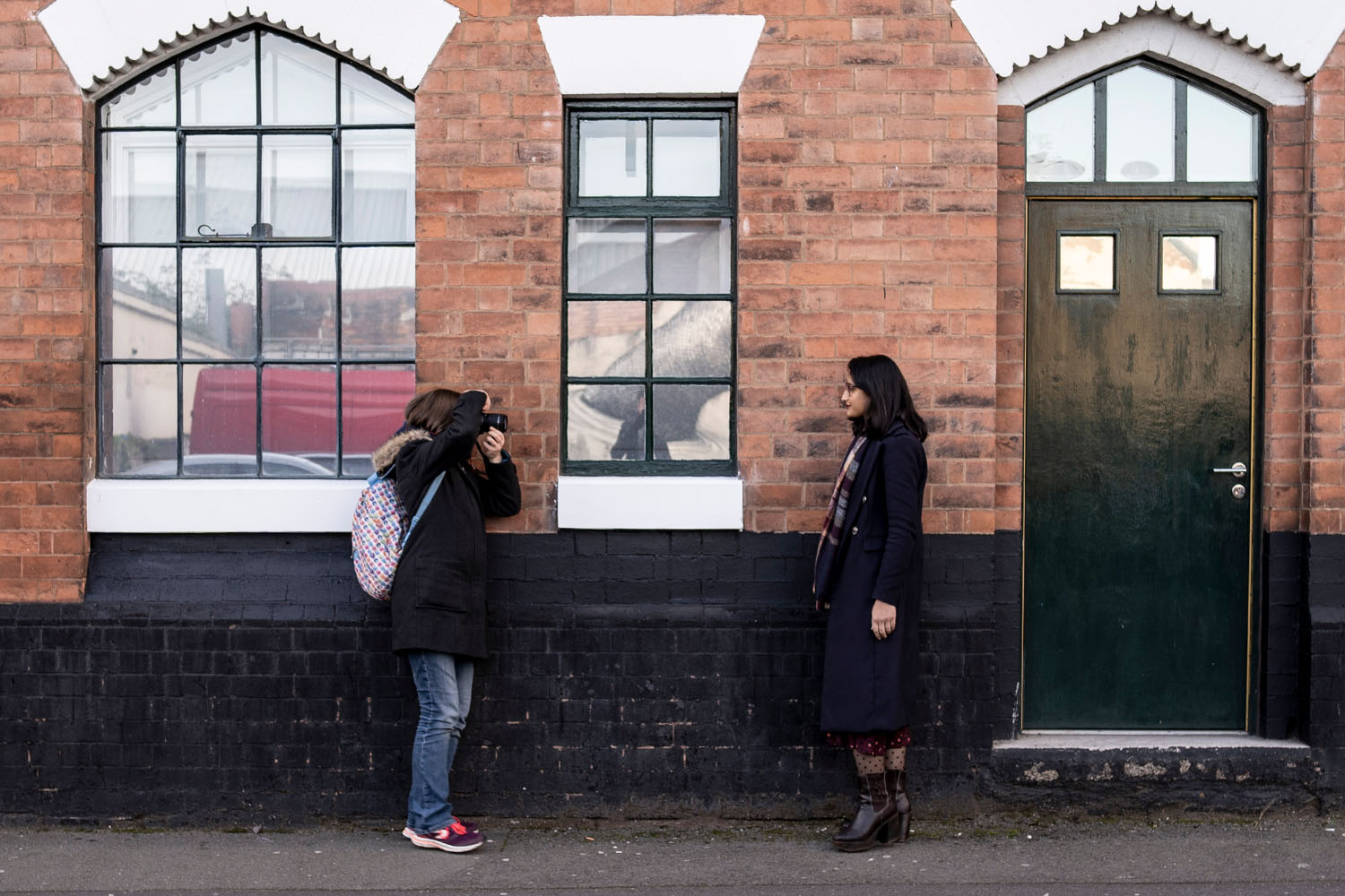 A woman taking a photo of a woman stood against a wall