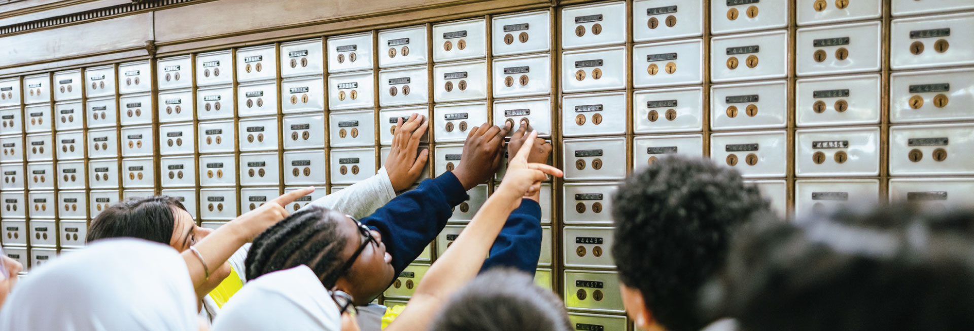 A group of school children reaches up to feel the locks on a wall of safe deposit boxes.