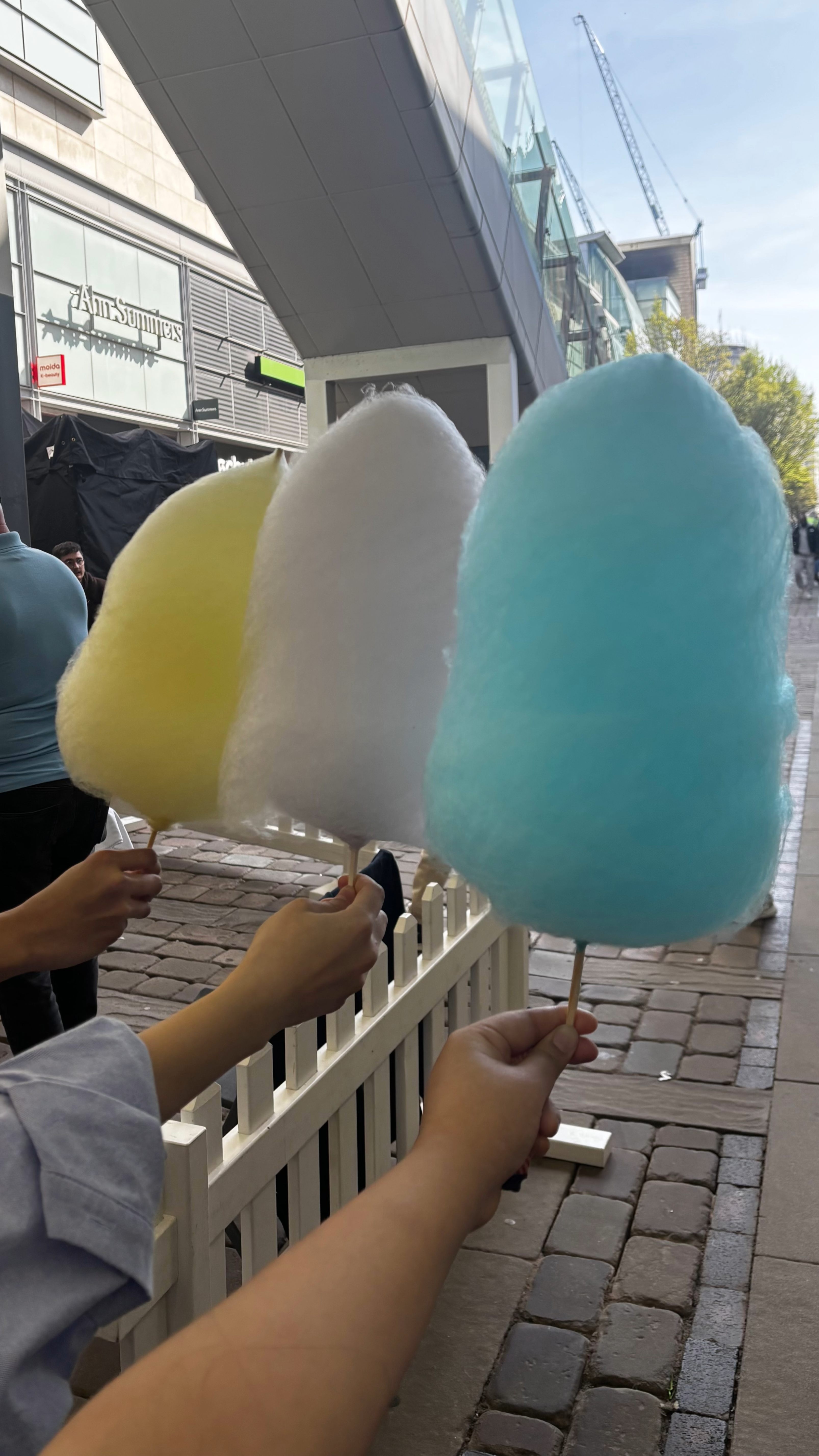 Three students holding three different coloured candy floss