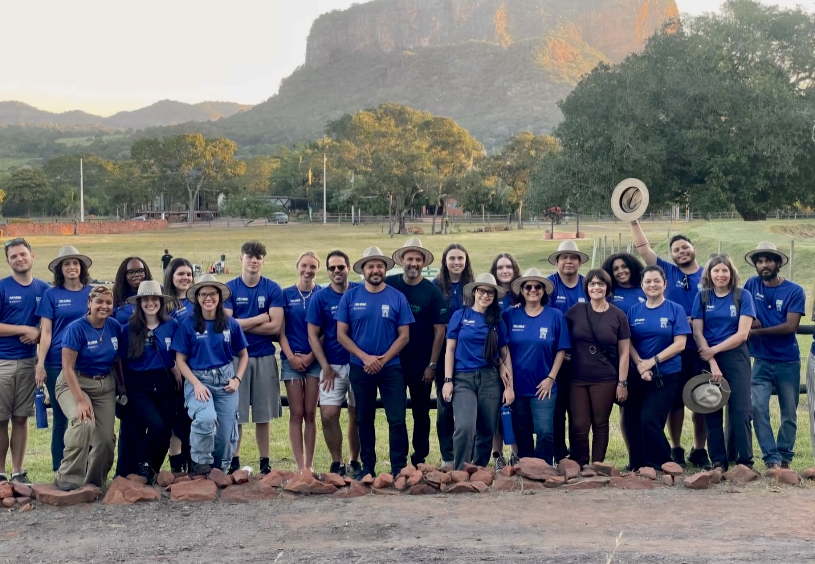 Academic and students cohort group wearing the programme blue shirt posing for a photo in front of a farm fence
