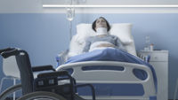 patient in hospital bed with neck brace, wheelchair in foreground 