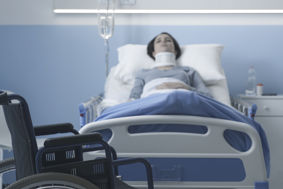 patient in hospital bed with neck brace, wheelchair in foreground 
