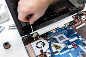Person holding a small screwdriver repairing the fan of laptop motherboard