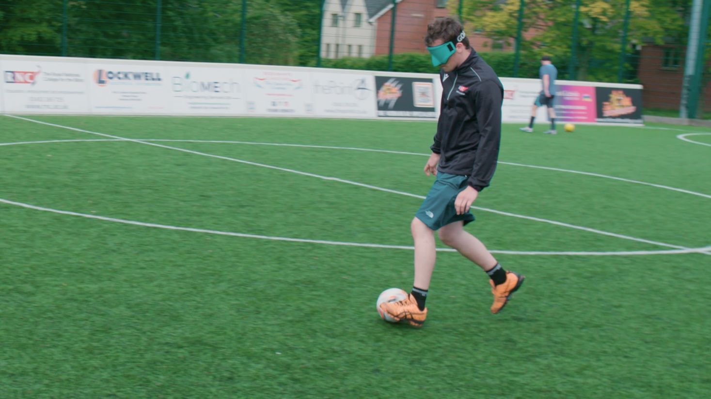 A young person with vision impairment playing football wearing a blindfold