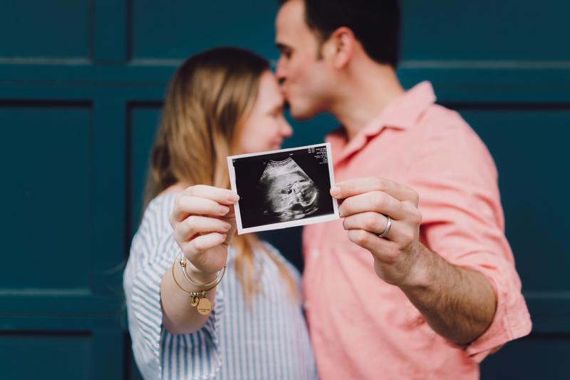 Man kissing pregnant woman's head while holding ultrasound picture of a baby