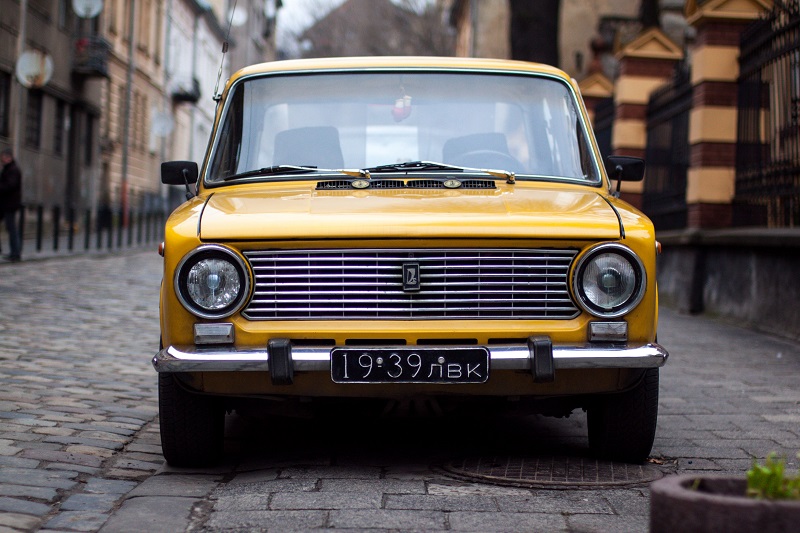 Mustard yellow Lada car with a Russian numberplate parked on a cobbled street