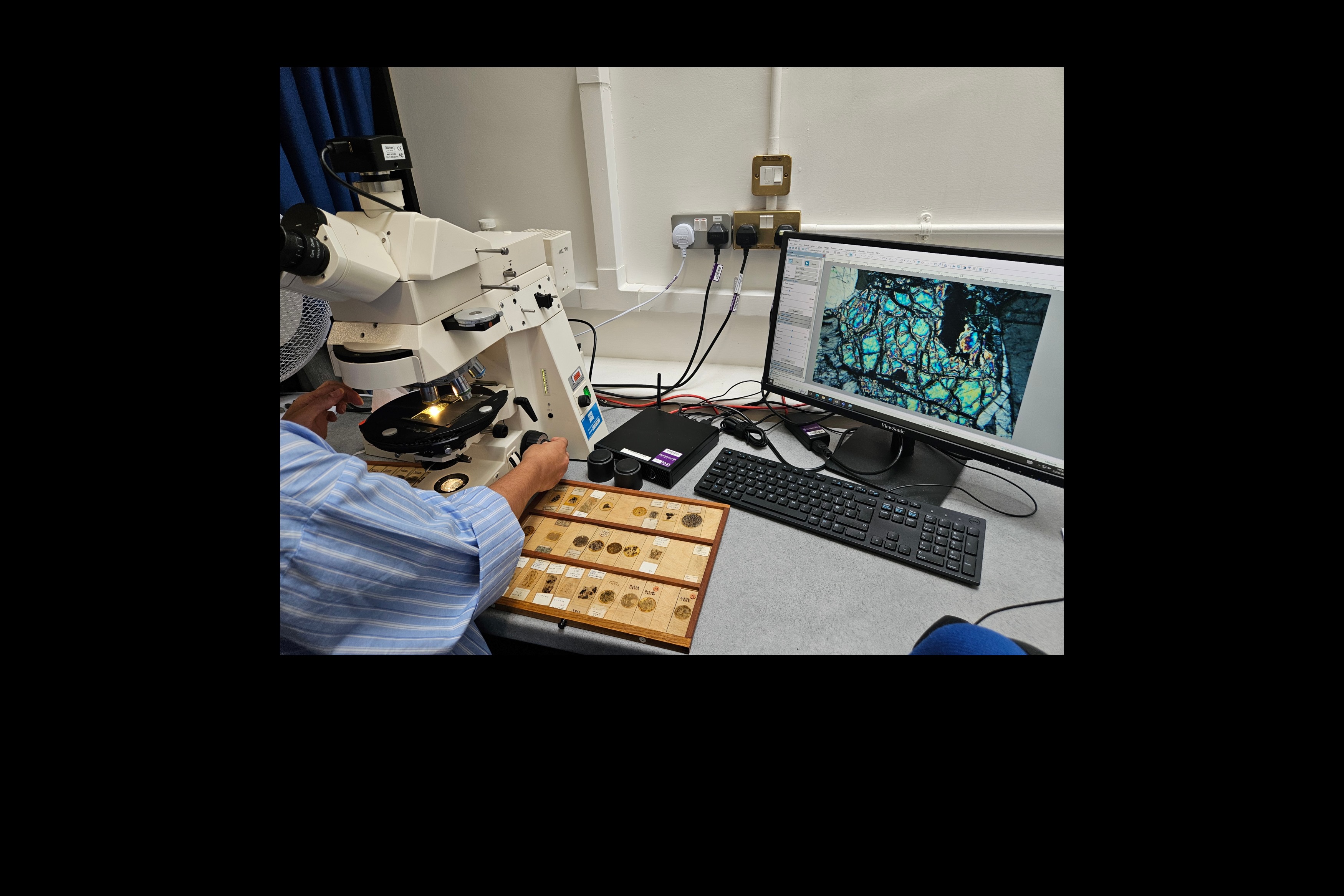 Adam examines a thin section under a microscope, with the image visualised on a monitor.