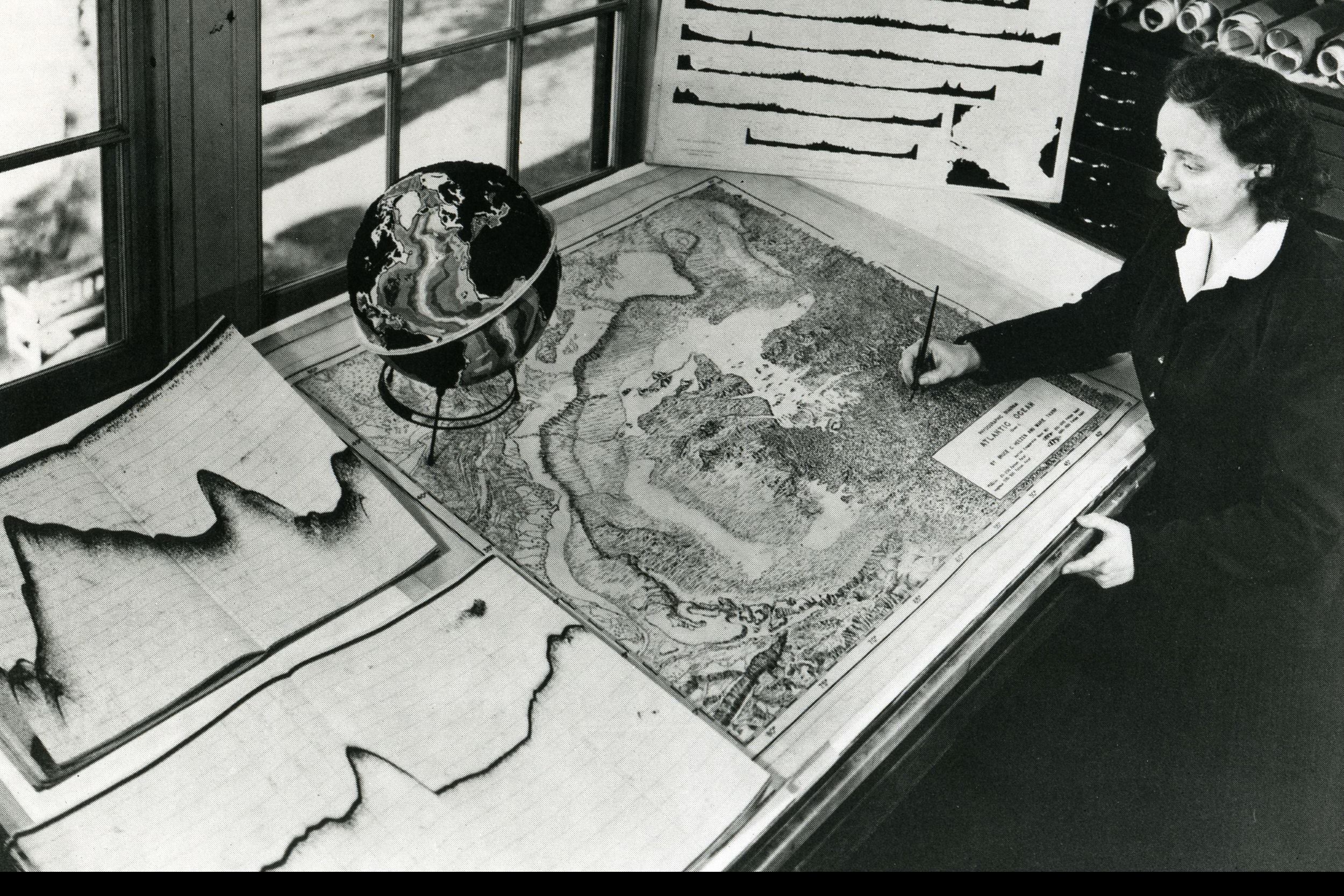 Black and white image where Marie Tharp works on a large map.
