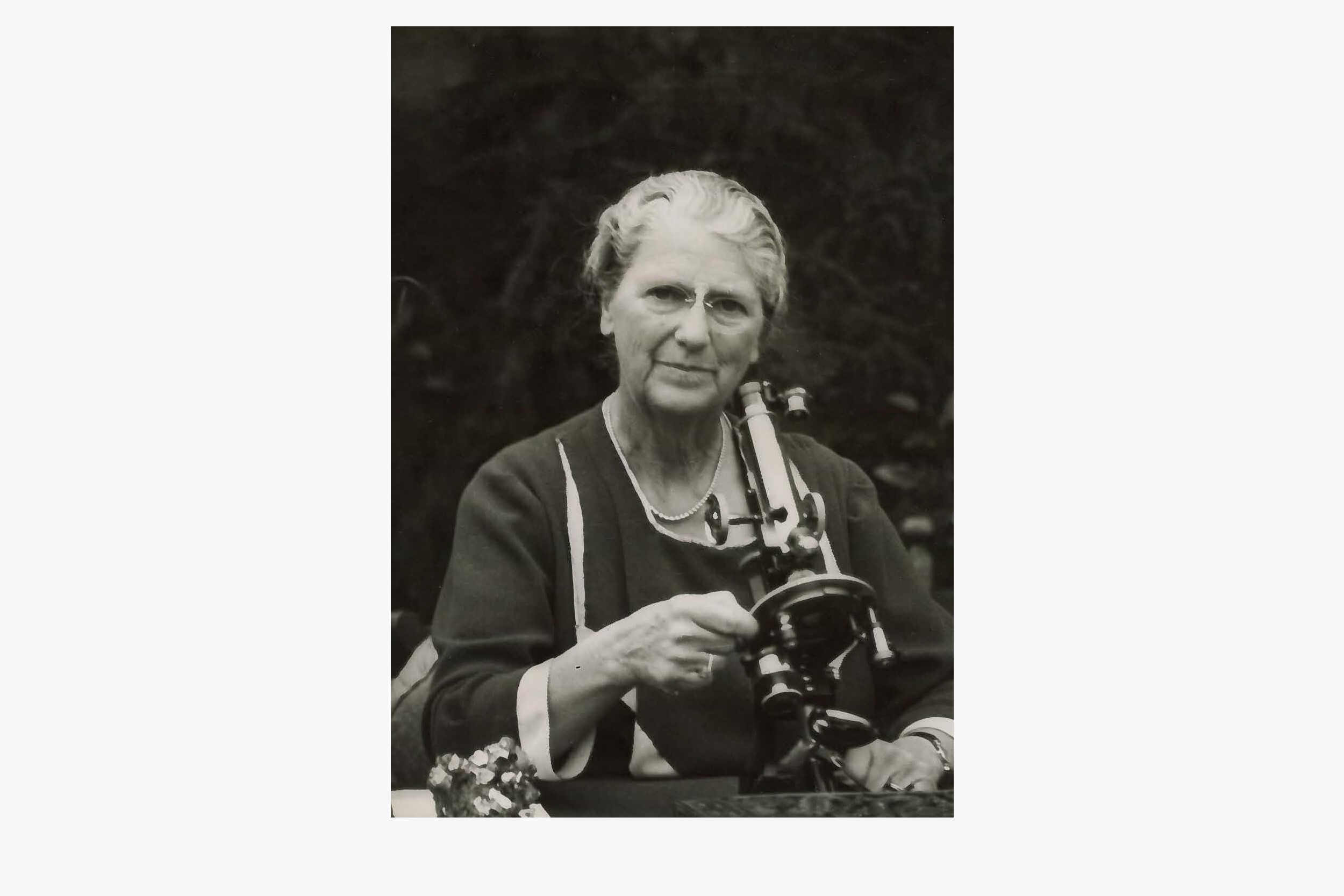A black and white photograph of Lady Rachel MacRobert with a microscope.