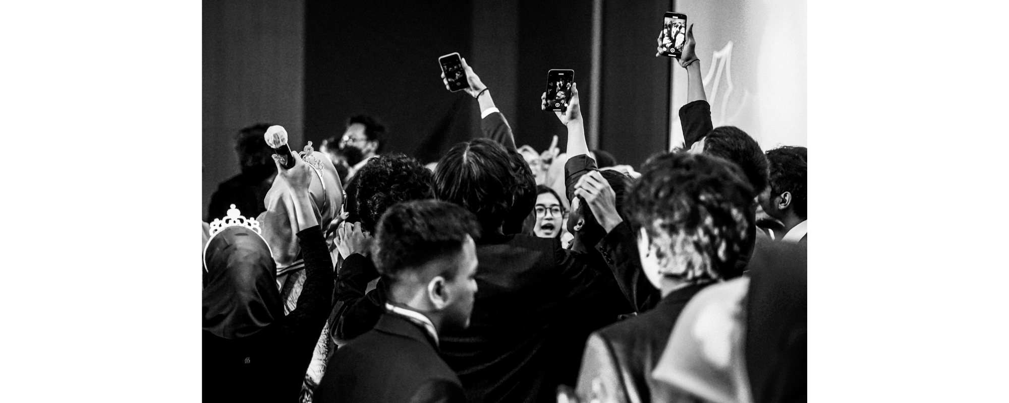 A crowd of people, 3 of which are filming something.