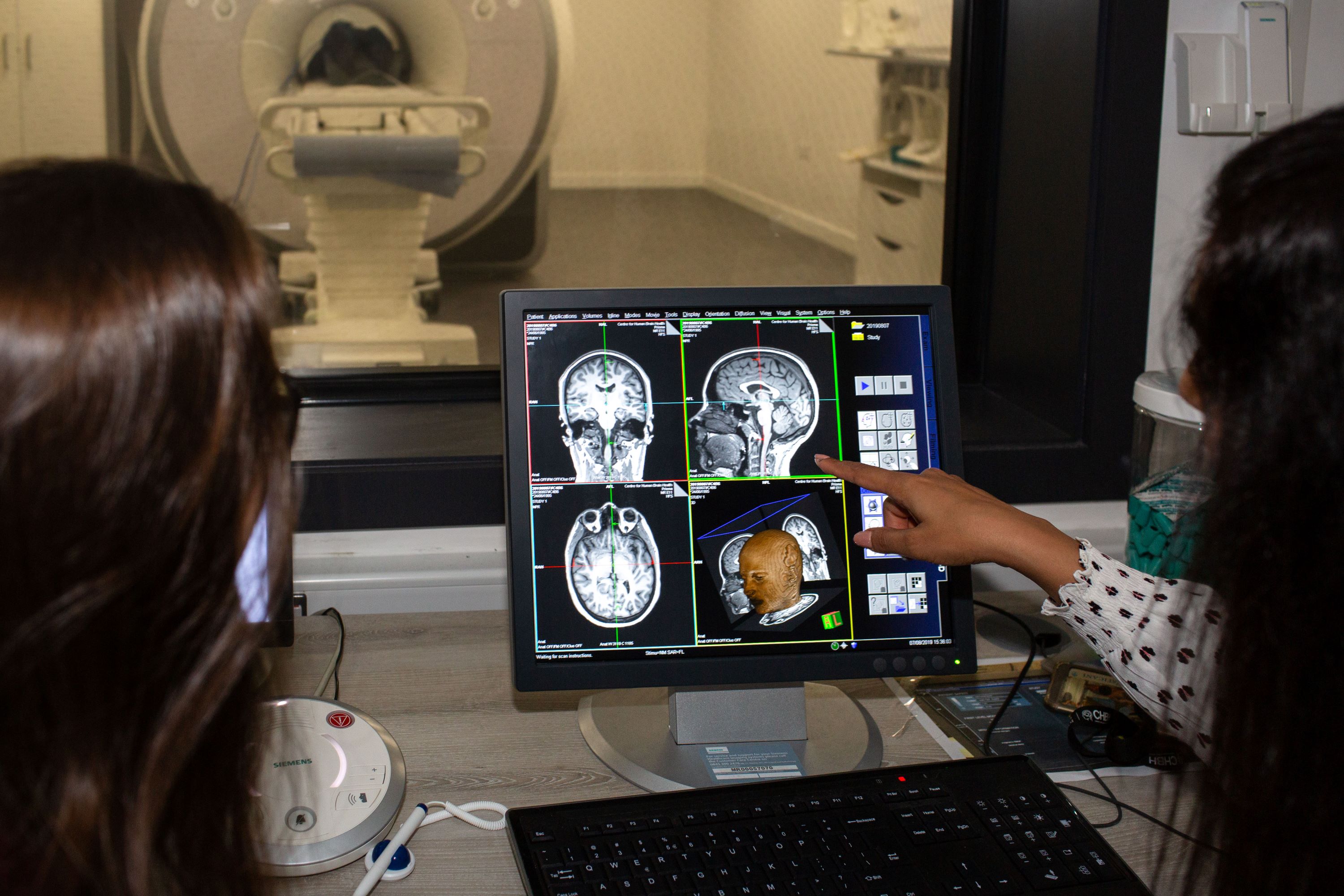 Two people viewing and discussing brain MRI scans on a computer near an MRI machine.