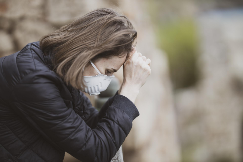 A pensive woman wearing face mask and resting her head on her hands