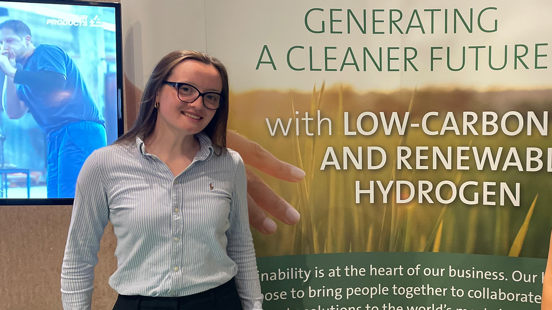 Maisie smiling and posing in front of an Air Products banner, during her placement year.