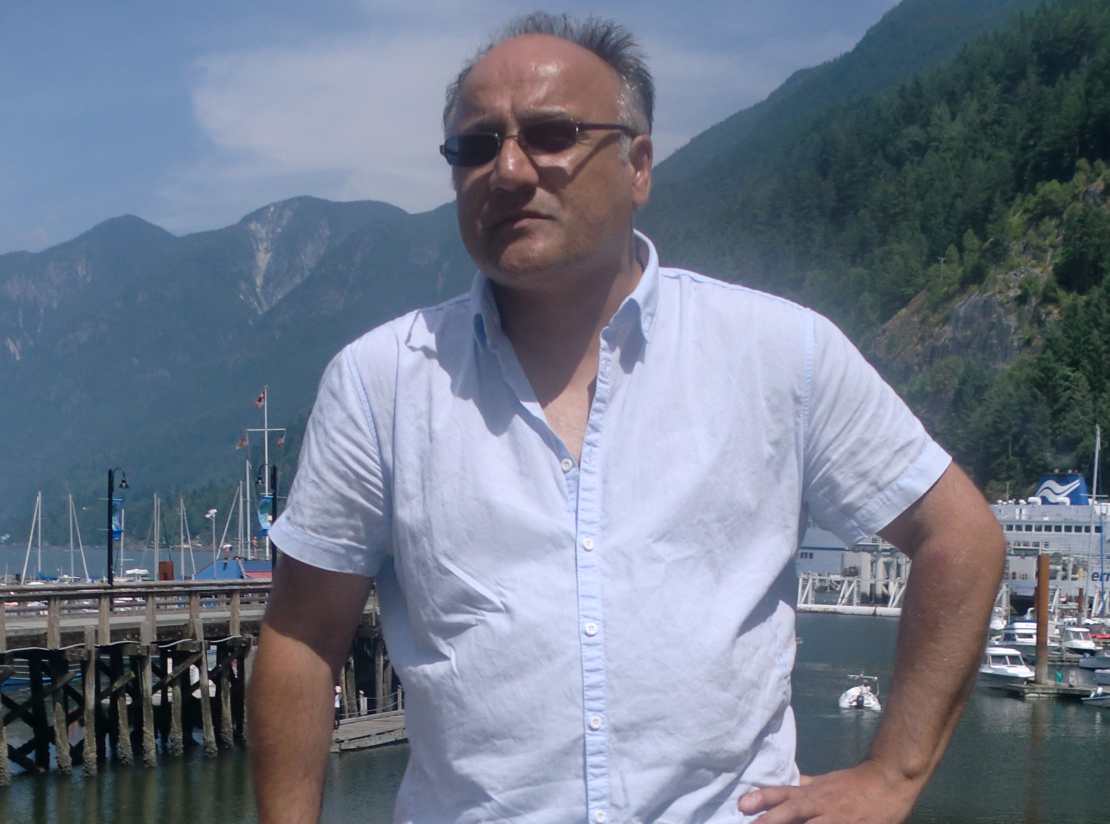 An older man wearing a shirt and glasses poses in a dock, on a sunny day