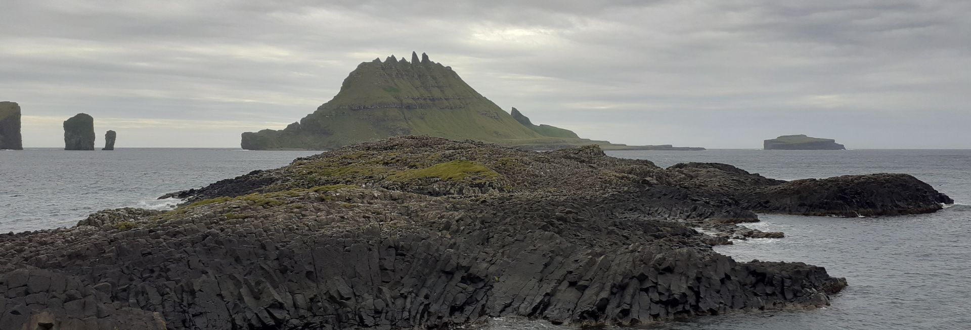 A photograph showing a remote landscape in the Faroe Islands with green mossy outcrops in a coastal area.