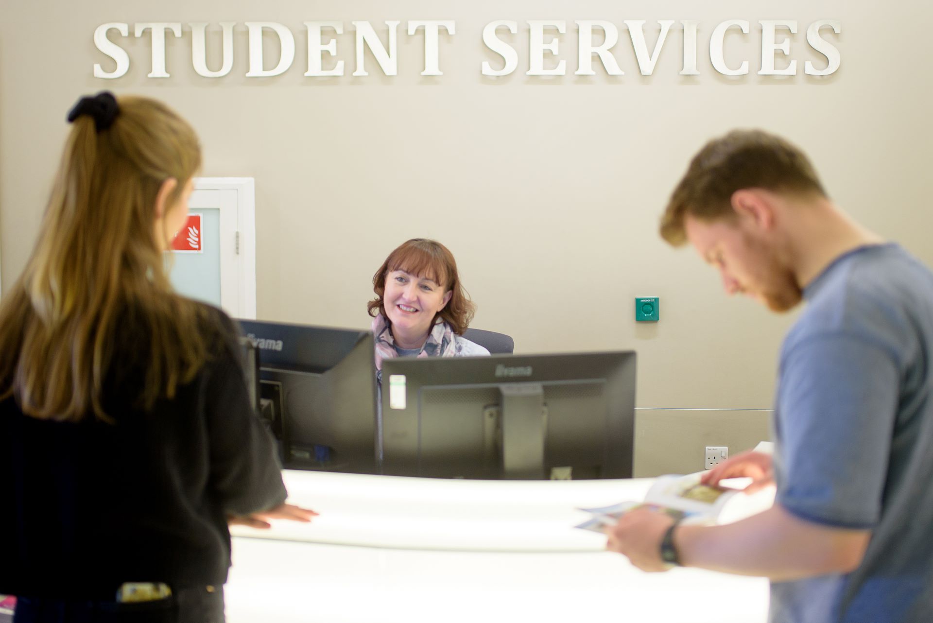 Staff on front desk of Medical School student services with two students waiting