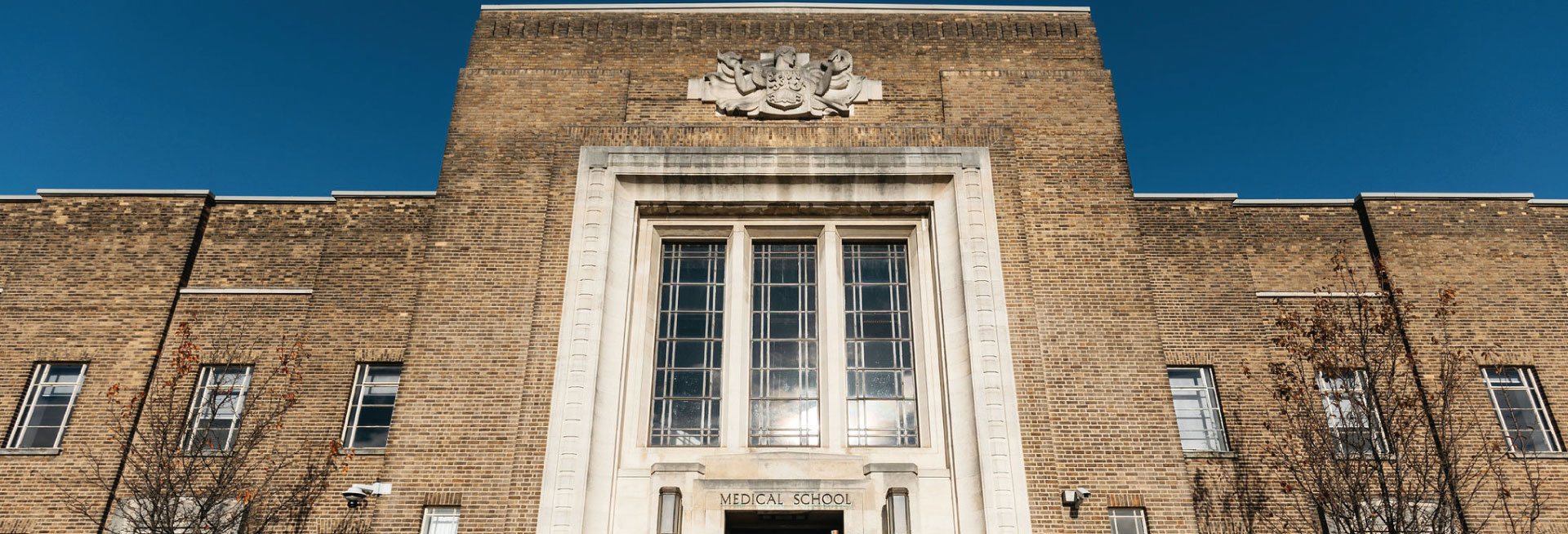 The exterior of Birmingham Medical School against a bright blue sky.