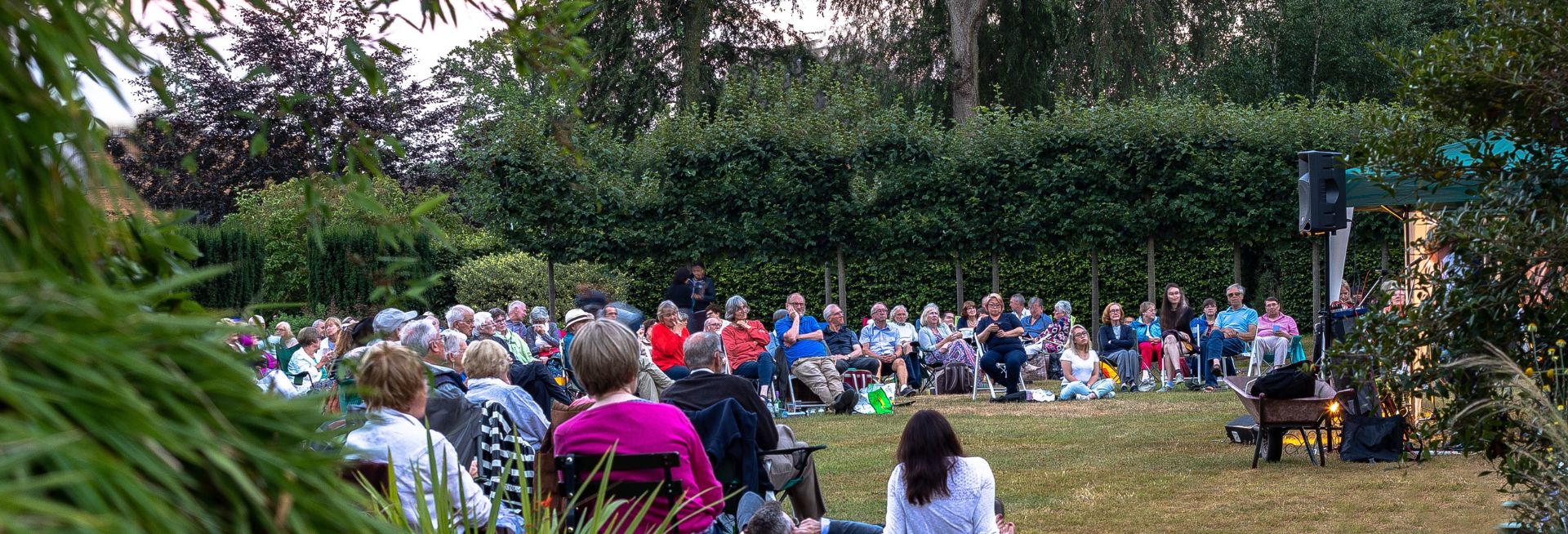 An audience sat on a lush green lawn watching a performance. 