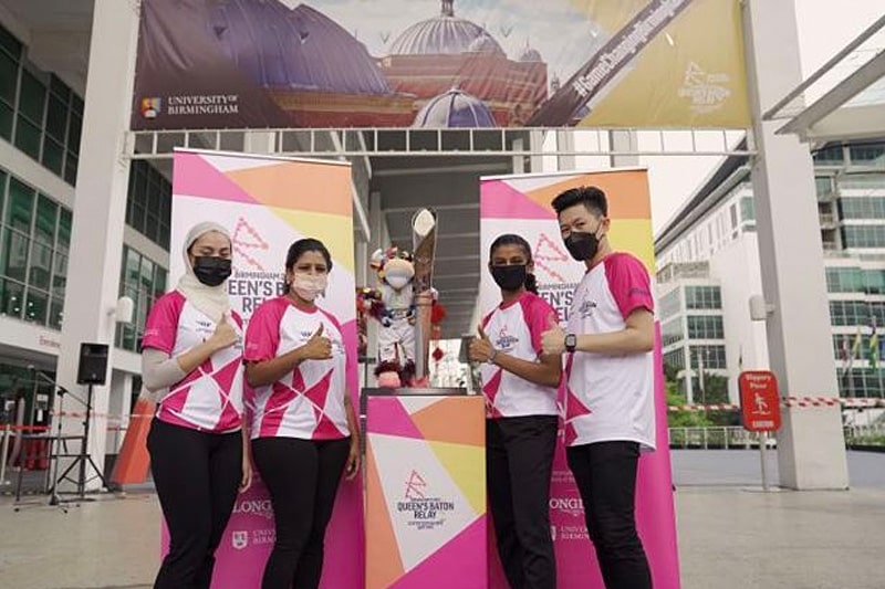 Four baton bearers in Malaysia giving a thumbs up next to the Commonwealth Games baton