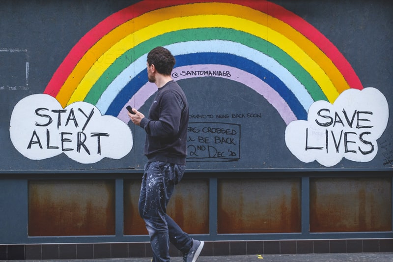 Man walking past a COVID rainbow mural bearing the words 'Stay Alert, Save Lives'
