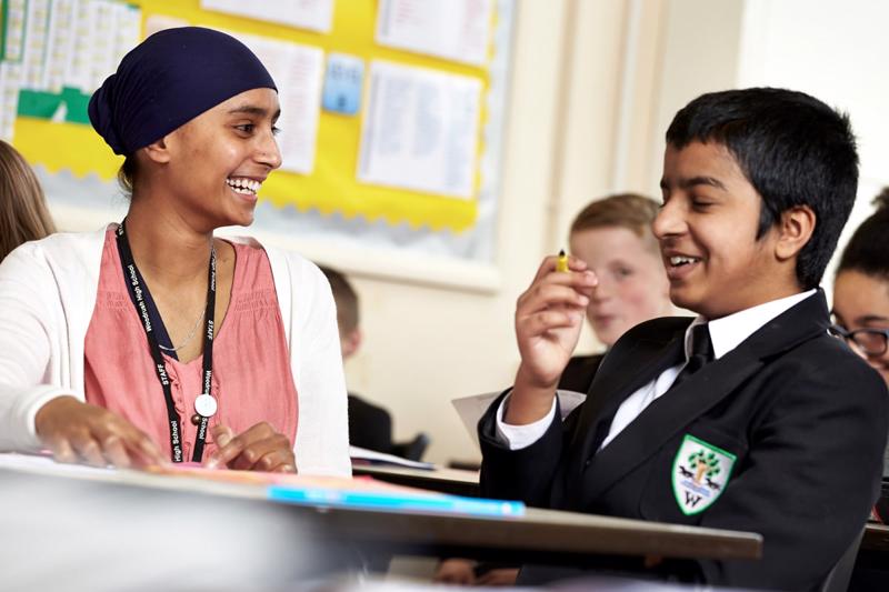 Female teacher laughing with a primary school pupil in the classroom.