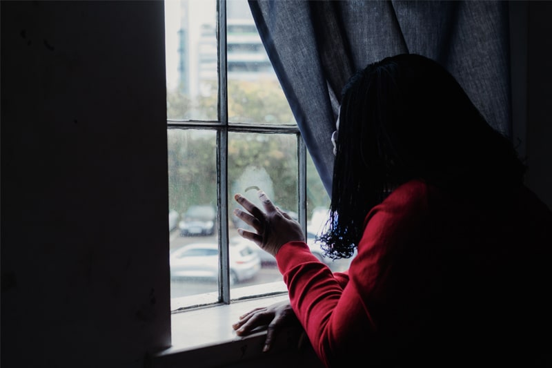 Oprah, an asylum seeker and victim of human trafficking, uses her finger to draw in the condensation on a window pane.