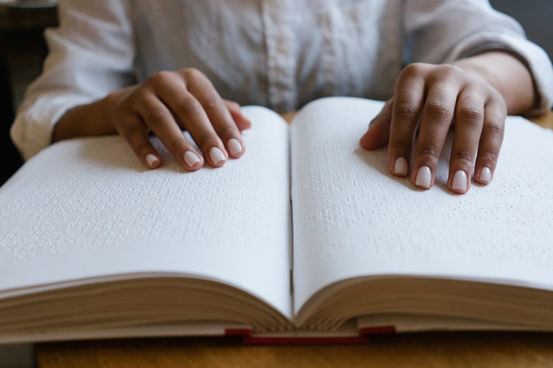 Hands reading the pages of a large braille book